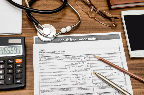 ziektekostenverzekering vorderingsformulier met stethoscoop op Klembord, spuit, rekenmachine en pen - Foto, afbeelding