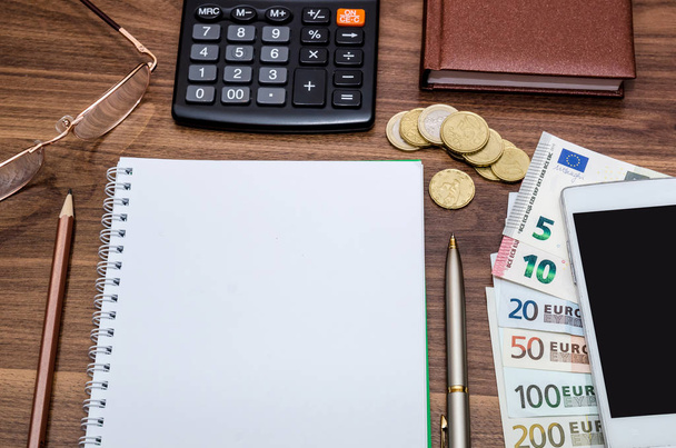 bloc de notas vacío con dinero en euros, móvil, calculadora y pluma en la mesa
 - Foto, imagen