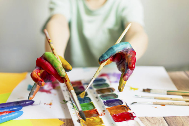 子供は絵を描く。多色の水彩画で子供の手のひらと手。水彩、ガッシュ、ペイントブラシ、色とワックスクレヨン、ステッカー。描画、創造性と趣味のためのセット - 写真・画像