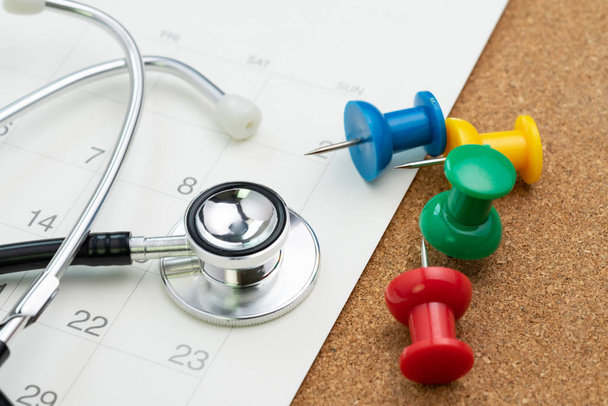 Schedule or appointment for medical exam or meet the doctor for health check up concept, colorful thumbtack or pushpin with white calendar and doctor stethoscope. - Fotografie, Obrázek