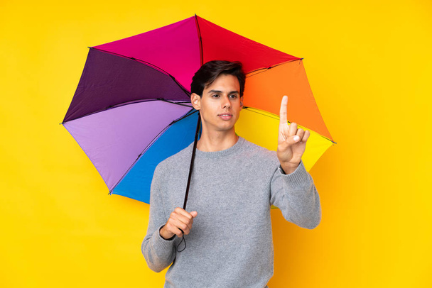 Homem segurando um guarda-chuva sobre fundo amarelo isolado tocando na tela transparente
 - Foto, Imagem