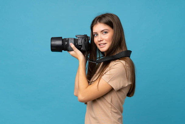 Νεαρή γυναίκα πάνω από απομονωμένο μπλε φόντο με μια επαγγελματική κάμερα - Φωτογραφία, εικόνα