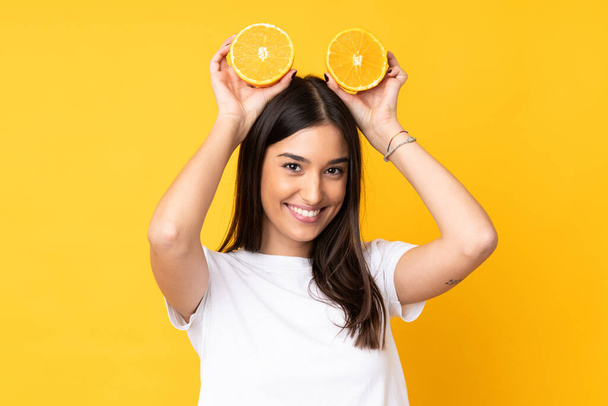 Young caucasian woman holding an orange over isolated yellow background - Fotografie, Obrázek