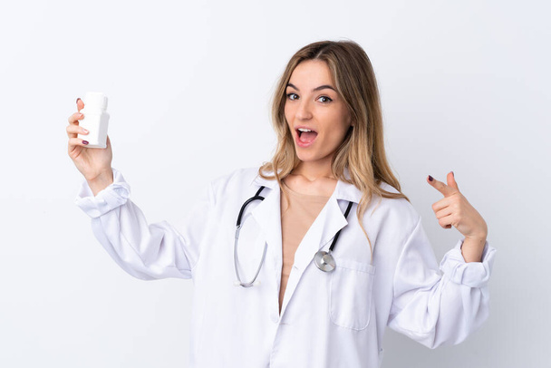 Young woman over isolated white background wearing a doctor gown and holding pills - Фото, зображення