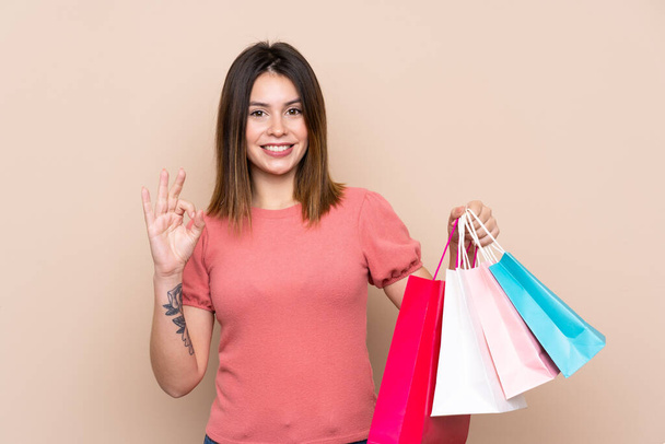 Молодая женщина с мешком для покупок на изолированном фоне показывает ОК знак с пальцами
 - Фото, изображение
