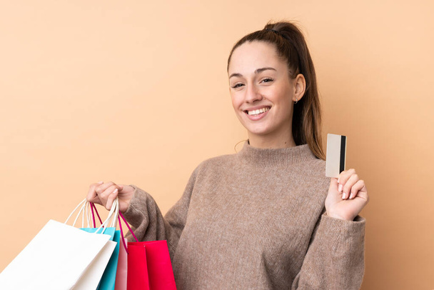 Young brunette woman over isolated background holding shopping bags and a credit card - Photo, Image