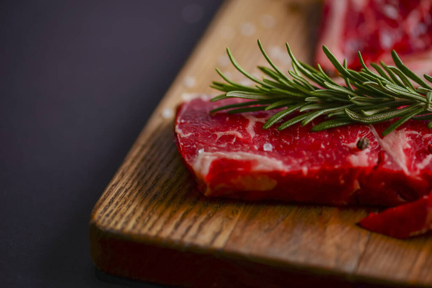 Fresh raw steak on wooden cutting board over black background with spices, top view. - Фото, изображение