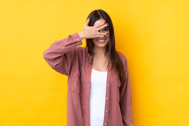 Giovane donna bruna su sfondo giallo isolato che copre gli occhi con le mani e sorridente
 - Foto, immagini