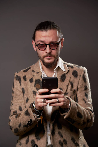 Male in sunglasses in jacket with phone in his hands on brown background - Foto, afbeelding