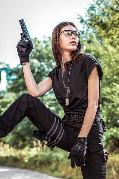 Dívka v taktickém oblečení se zbraní. Vojenská žena. Černé tričko a kalhoty. Pouzdro. SWAT - Fotografie, Obrázek