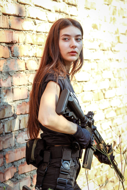 Dziewczyna w taktycznym ubraniu z bronią. Wojskowa kobieta. Czarna koszulka i spodnie. Kabura .SWAT - Zdjęcie, obraz