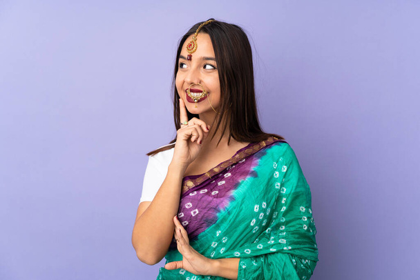 jonge Indiase vrouw geïsoleerd op paarse achtergrond denken een idee terwijl op zoek omhoog - Foto, afbeelding