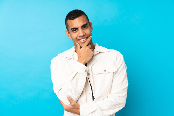 Jonge Afro-Amerikaanse man over geïsoleerde blauwe achtergrond glimlachen - Foto, afbeelding