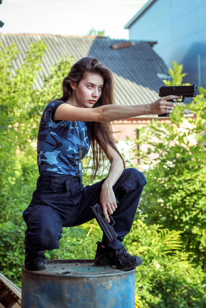 Chica con ropa táctica con un arma. Mujer militar. Camiseta azul camuflaje y bolsa con dos pistolas. Prendas civiles
. - Foto, imagen