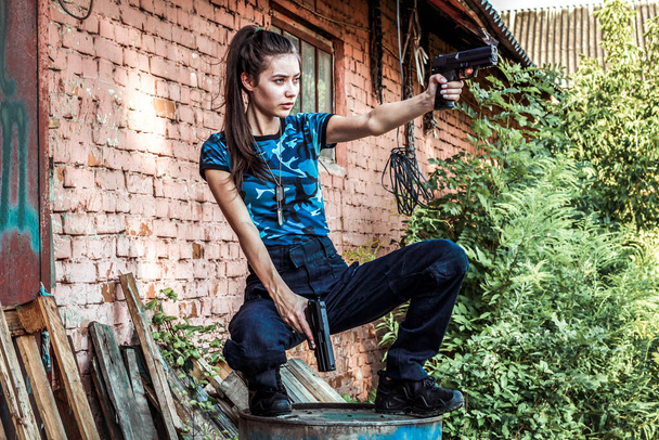 Taktikai ruhás lány fegyverrel. Katonai nő. Kék terepszínű póló és táska két pisztollyal. Polgári ruházat. - Fotó, kép