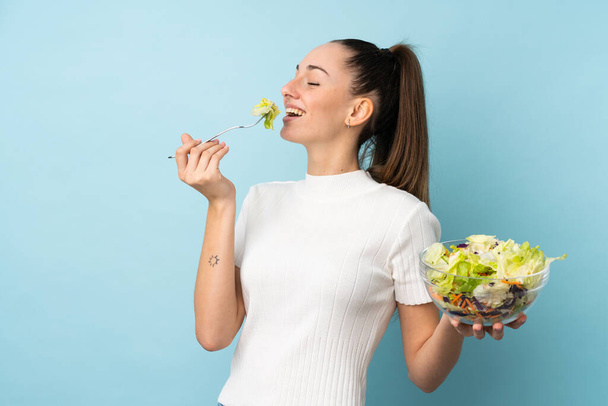 junge brünette Frau mit einem Salat vor isoliertem blauen Hintergrund - Foto, Bild