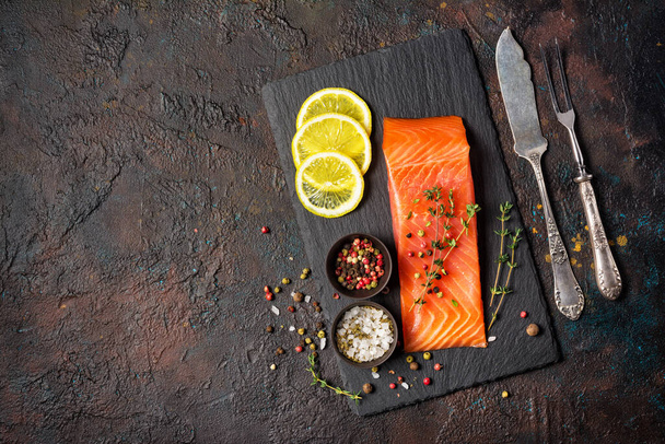 Top view of cold smoked trout fillet with thyme and silver cutlery on shale board and dark grunge background with copy space - Foto, Imagem