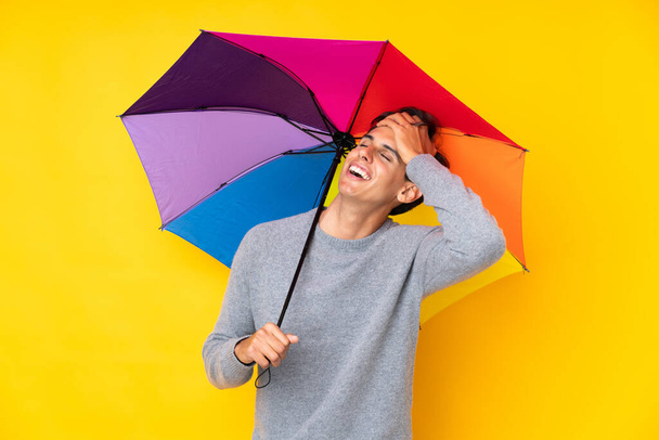Man holding an umbrella over isolated yellow background laughing - Photo, image