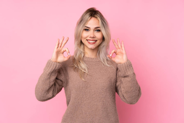 Adolescente rubia chica usando un suéter sobre aislado rosa fondo mostrando un signo de ok con los dedos
 - Foto, imagen