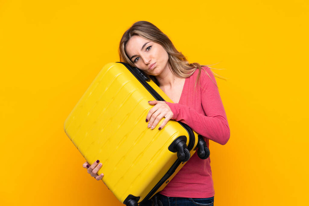Young woman over isolated yellow background in vacation with travel suitcase and unhappy - Photo, image