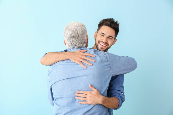 Young man and his father hugging on color background - Photo, Image