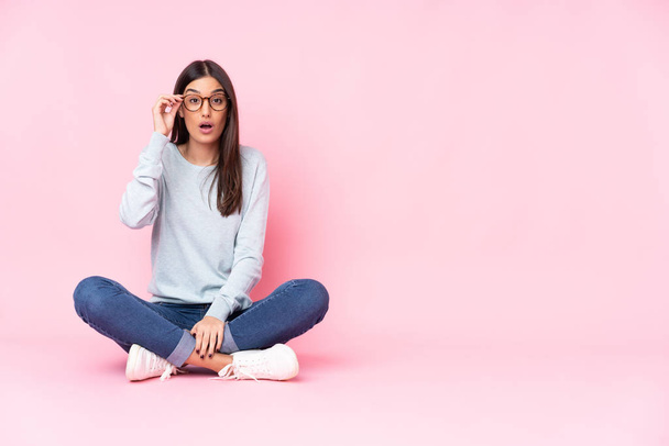 Young caucasian woman isolated on pink background with glasses and surprised - Photo, Image