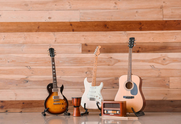 Современные гитары, барабан и радиоприемник возле деревянной стены
 - Фото, изображение