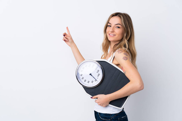 Молодая женщина на изолированном белом фоне с весовым механизмом и указательной стороной - Фото, изображение