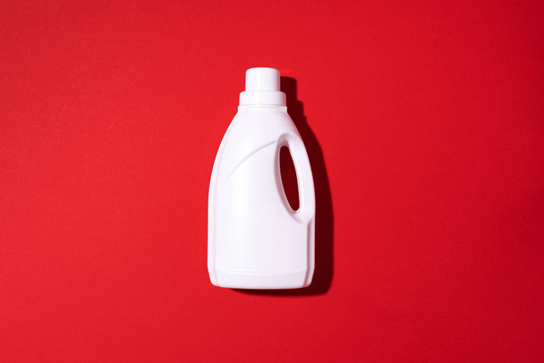 White plastic bottle of cleaning product, household chemicals or liquid laundry detergent on red background. Top view. Flat lay. Copy space. Detergent bottle - Photo, Image