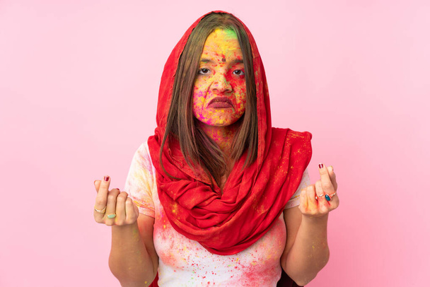 Young Indian woman with colorful holi powders on her face isolated on pink background making money gesture but is ruined - Foto, Bild