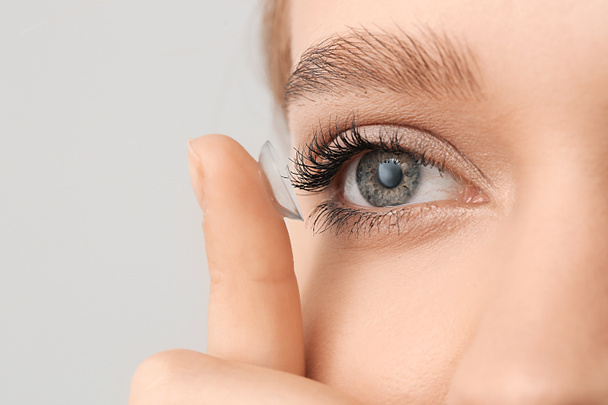 Young woman with contact lens on grey background, closeup - Fotoğraf, Görsel