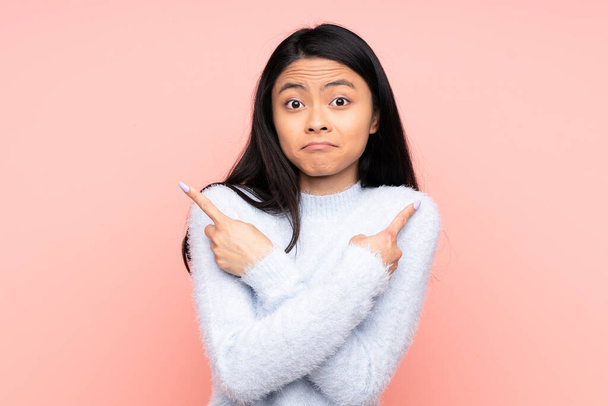 Teenager Chinese woman isolated on pink background pointing to the laterals having doubts - Foto, immagini