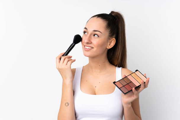 jong brunette vrouw over geïsoleerde wit achtergrond met make-up palet en gelukkig - Foto, afbeelding