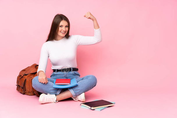 Teenager caucasian student girl sitting on the floor isolated on pink background doing strong gesture - Foto, Imagem