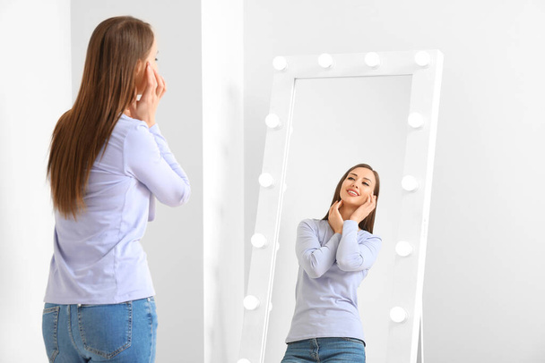Beautiful young woman looking in mirror at home - Photo, Image