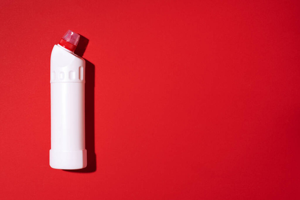 Λευκό πλαστικό μπουκάλι του προϊόντος καθαρισμού, οικιακές χημικές ουσίες ή υγρό απορρυπαντικό πλυντηρίου σε κόκκινο φόντο. Στο πάνω μέρος. Επίπεδη. Αντιγραφή χώρου. Φιάλη απορρυπαντικού - Φωτογραφία, εικόνα
