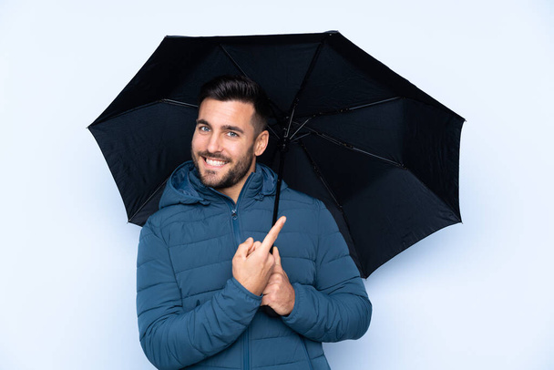 Άντρας κρατώντας μια ομπρέλα πάνω από απομονωμένο φόντο και δείχνοντας το - Φωτογραφία, εικόνα