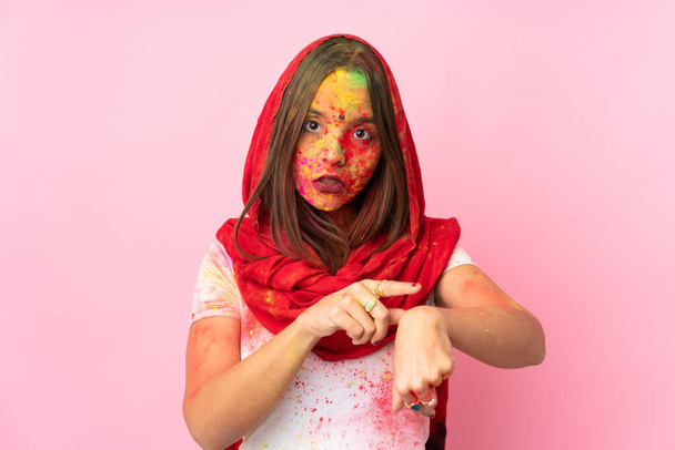 Young Indian woman with colorful holi powders on her face isolated on pink background making the gesture of being late - Фото, изображение
