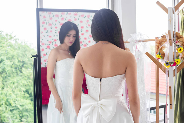 Отражение в зеркале азиатской невесты на свадебном платье в магазине
. - Фото, изображение
