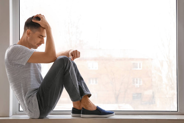 Depressed young man near window - Photo, Image