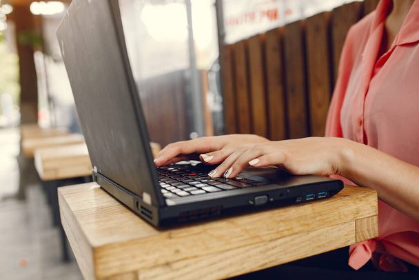 Дівчина в рожевій сорочці сидить за столом і використовує ноутбук
 - Фото, зображення