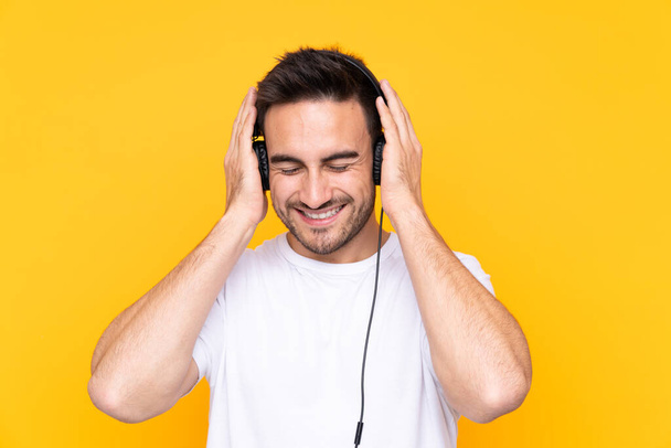 Young man over yellow background listening music - Fotó, kép