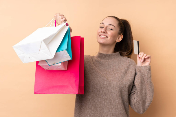 Молодая брюнетка на изолированном фоне держит сумки с покупками и кредитку
 - Фото, изображение