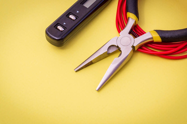 Electrician's tools and wire on a yellow background for repairing energized systems or communications - Foto, Imagen