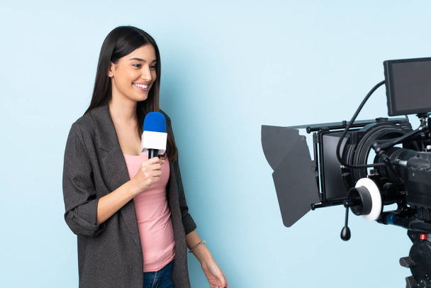 Reporter woman holding a microphone and reporting news isolated on blue background - Photo, Image