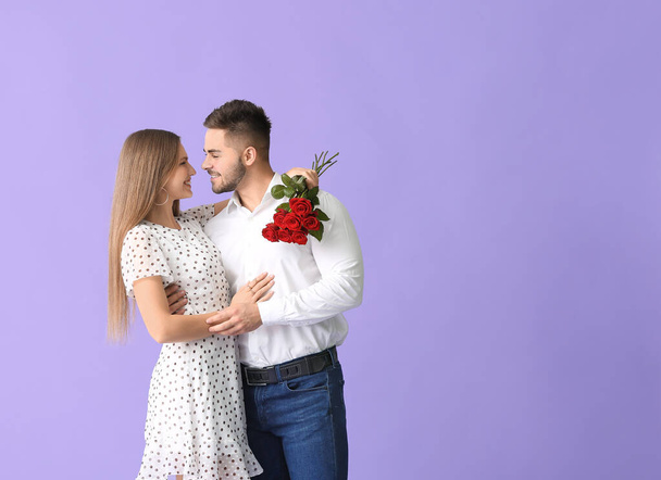 Ευτυχισμένο νεαρό ζευγάρι με μπουκέτο λουλούδια στο φόντο χρώμα - Φωτογραφία, εικόνα