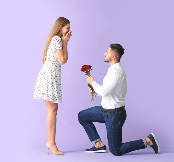 Glücklicher Mann gibt Blumenstrauß für seine Freundin auf farbigem Hintergrund - Foto, Bild