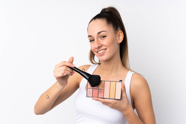Mladá brunetka žena přes izolované bílé pozadí s make-up paleta a šťastný - Fotografie, Obrázek
