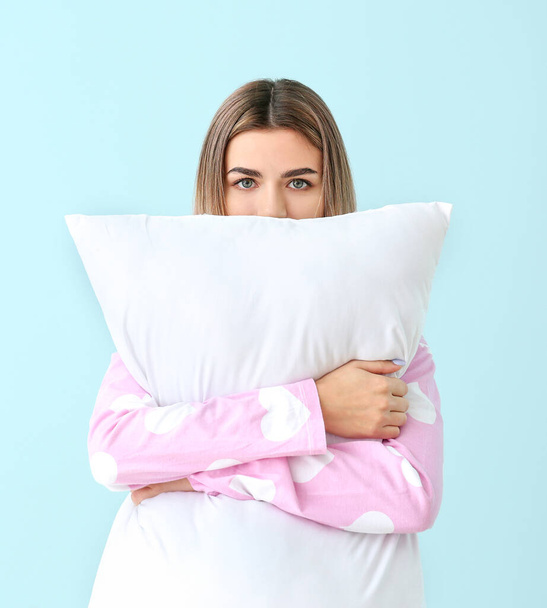Portrait of young woman in pajamas and with pillow on color background - Photo, image