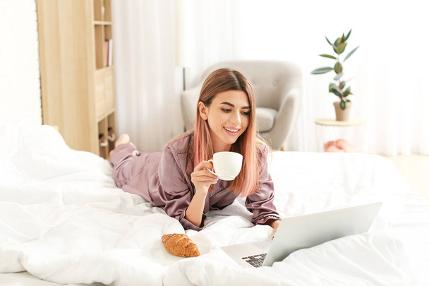 Hermosa joven con portátil y taza de café en la cama
 - Foto, imagen